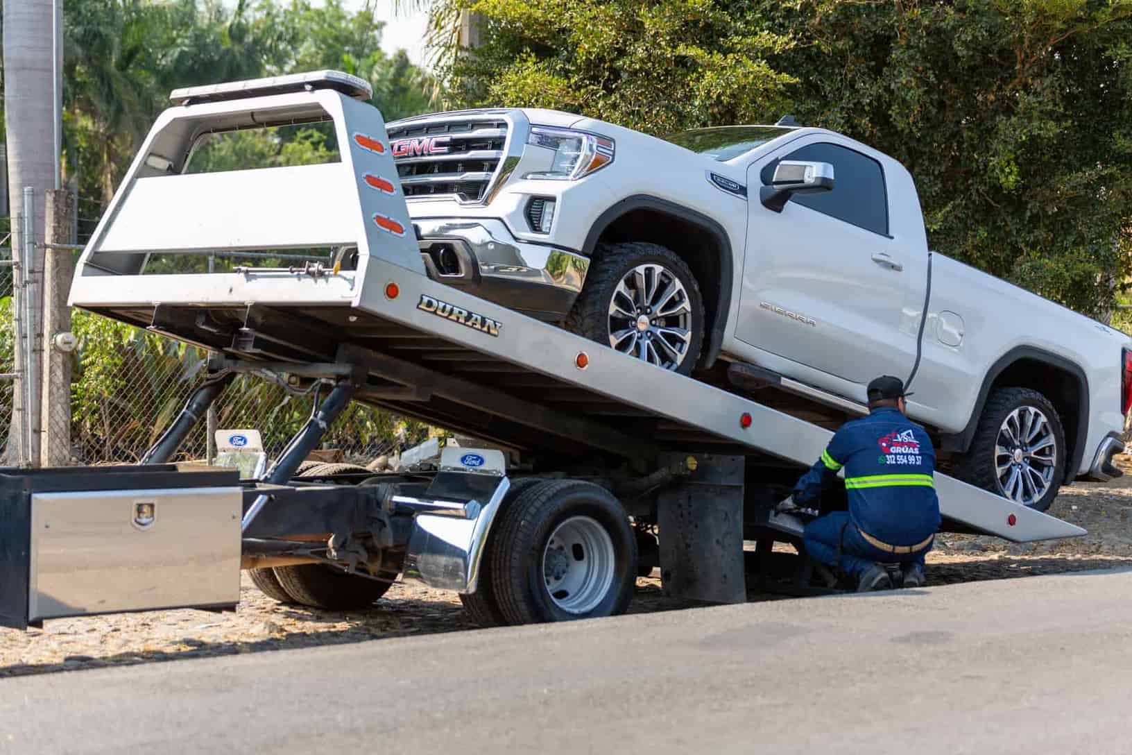 Tow truck operator loading white GMC pickup truck on street in daytime