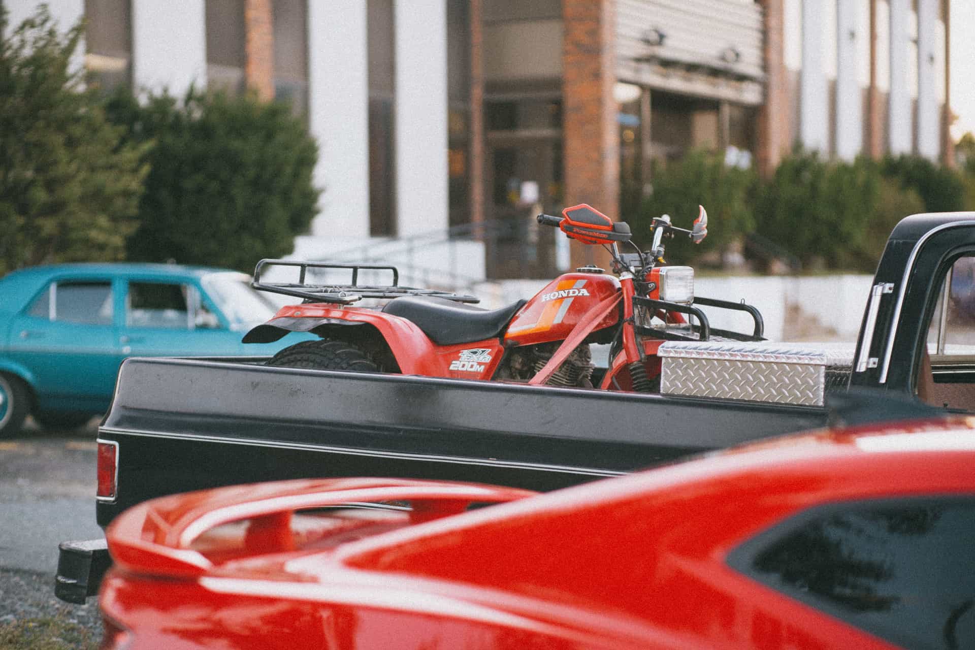 Red Honda ATV loaded on a black pickup truck parked in an urban environment