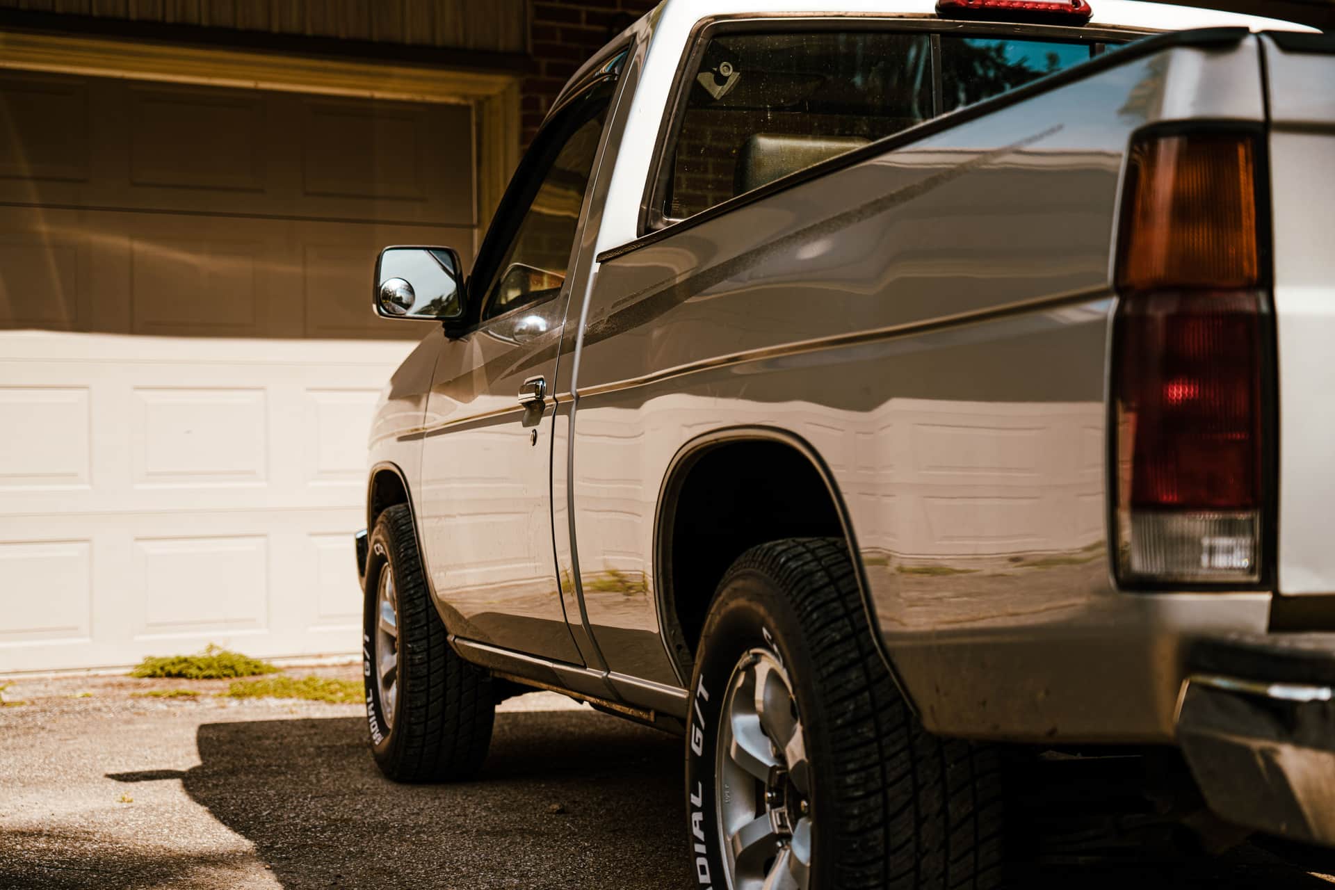 A silver pickup truck parked in a sunny residential driveway with closed garage doors