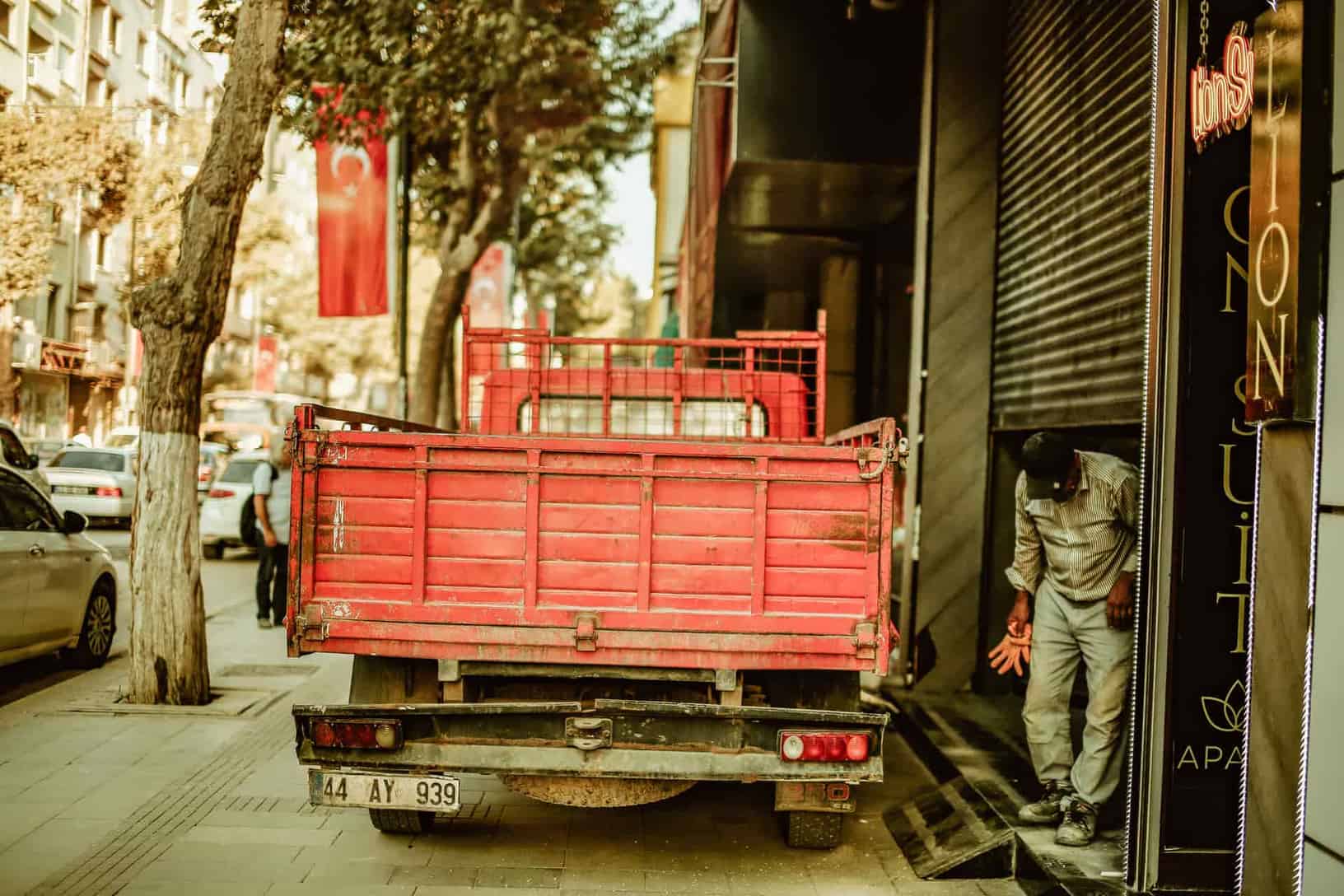 A red delivery truck parked on a city street with a worker nearby during the day