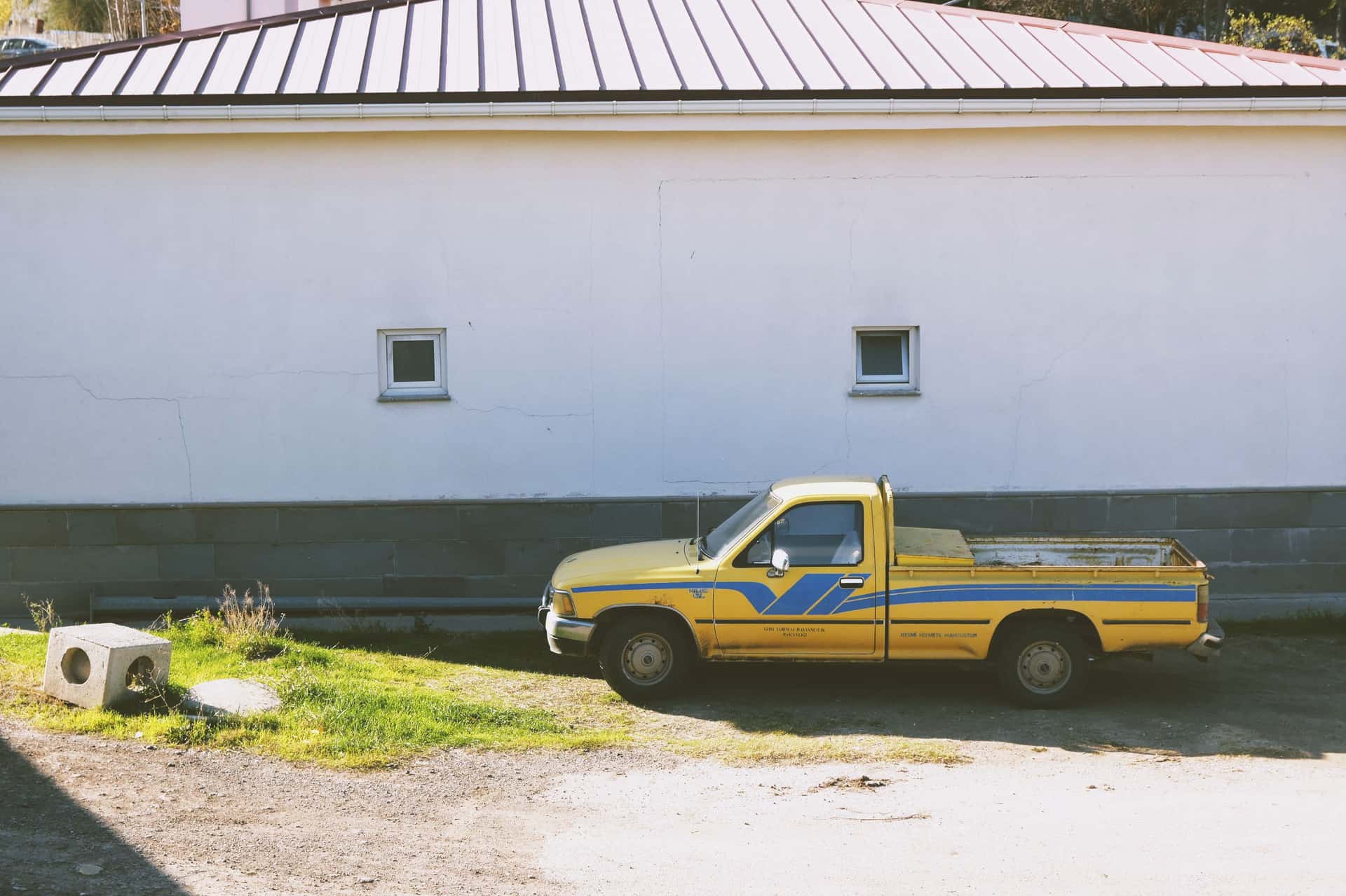 A vintage yellow truck parked next to a white wall on a sunny day