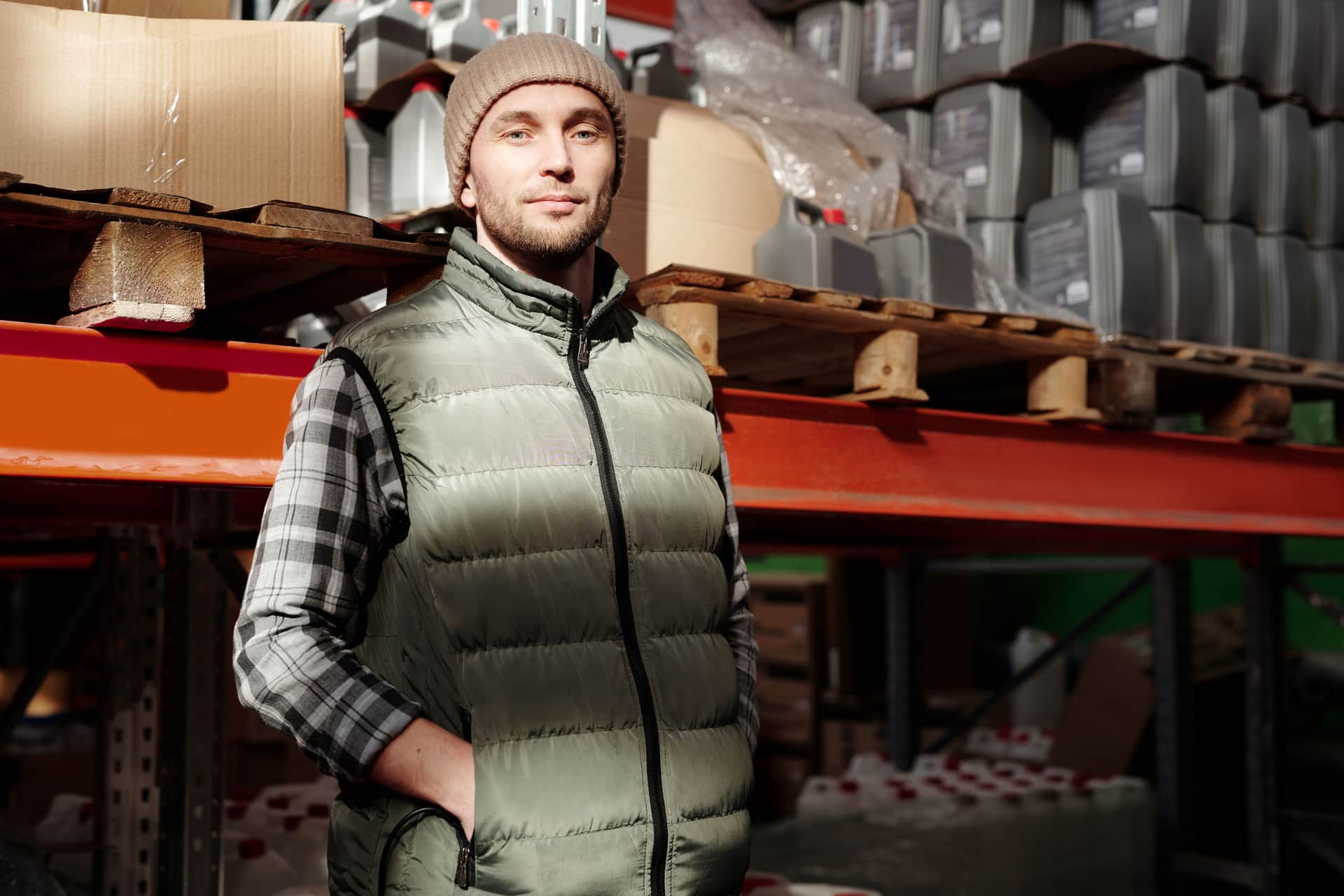 A man in a green vest stands confidently in a warehouse, illuminated by natural light