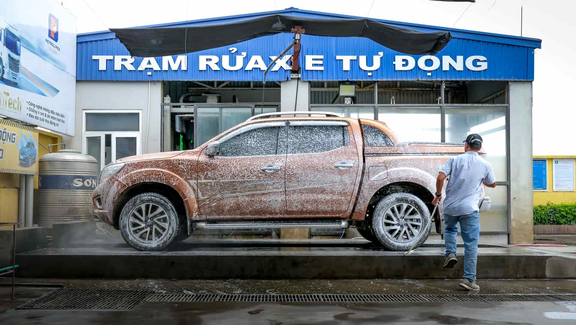 A man cleans a foamy pickup truck at an automatic car wash station outdoors