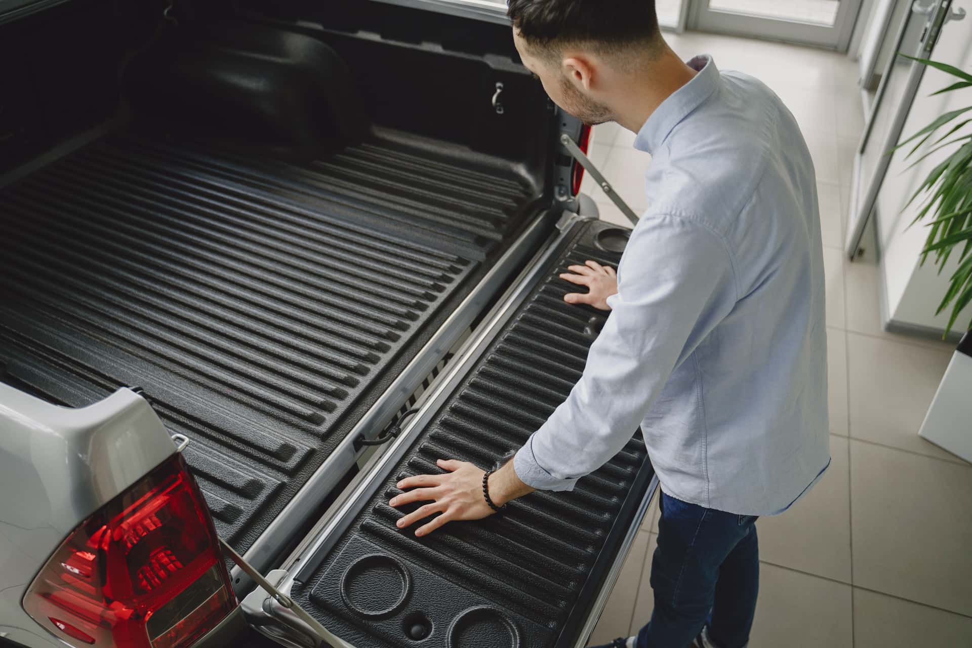 Adult man examines tailgate of a new pickup truck in a vehicle showroom
