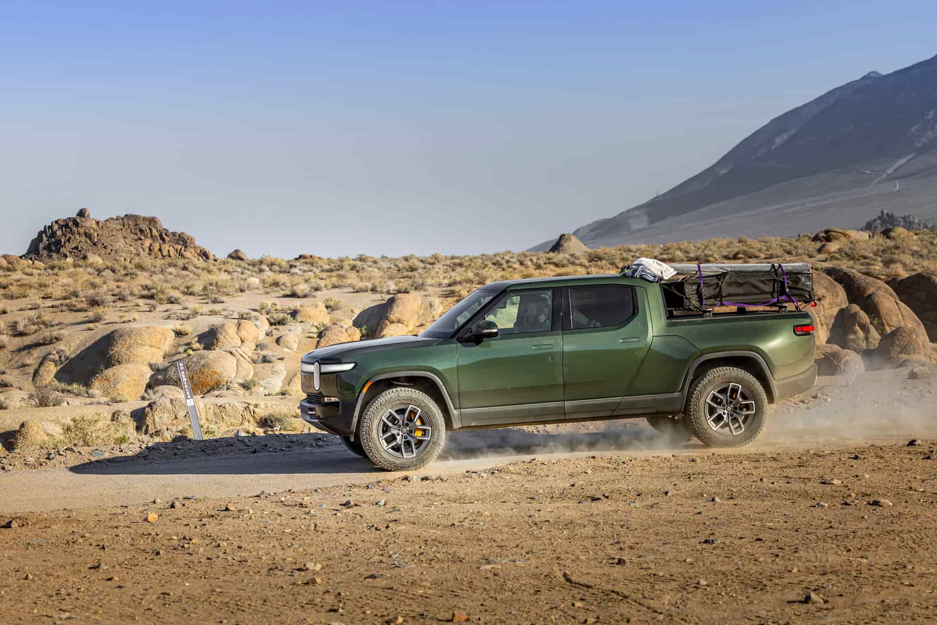 Green electric pickup truck on a dusty trail in a rocky desert landscape
