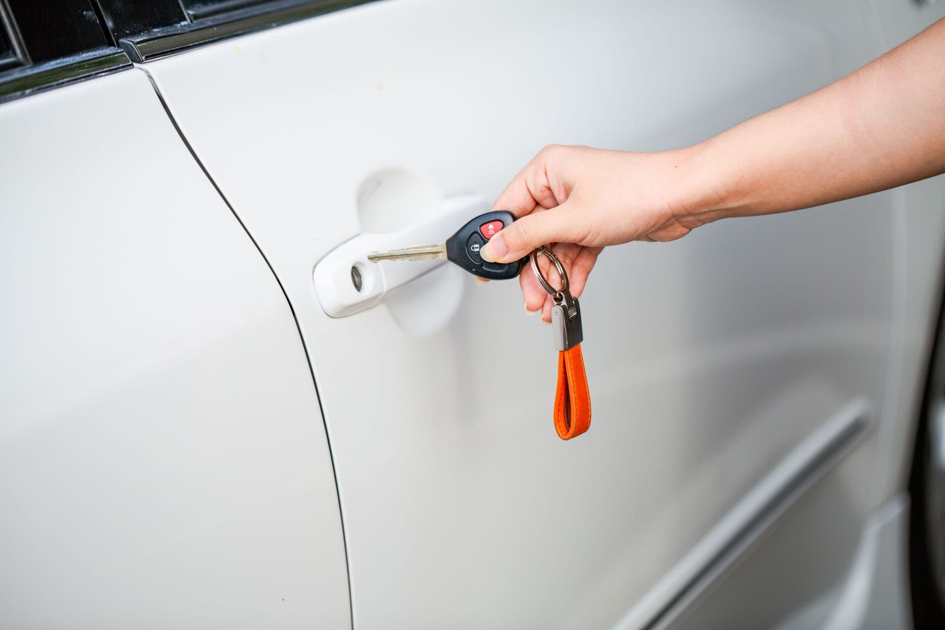 Close-up of a hand unlocking a white car door with a metal key and key fob