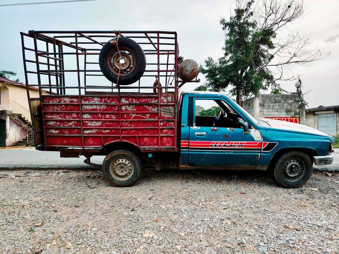 Old blue and red pickup truck with a metal cage parked on a gravel road