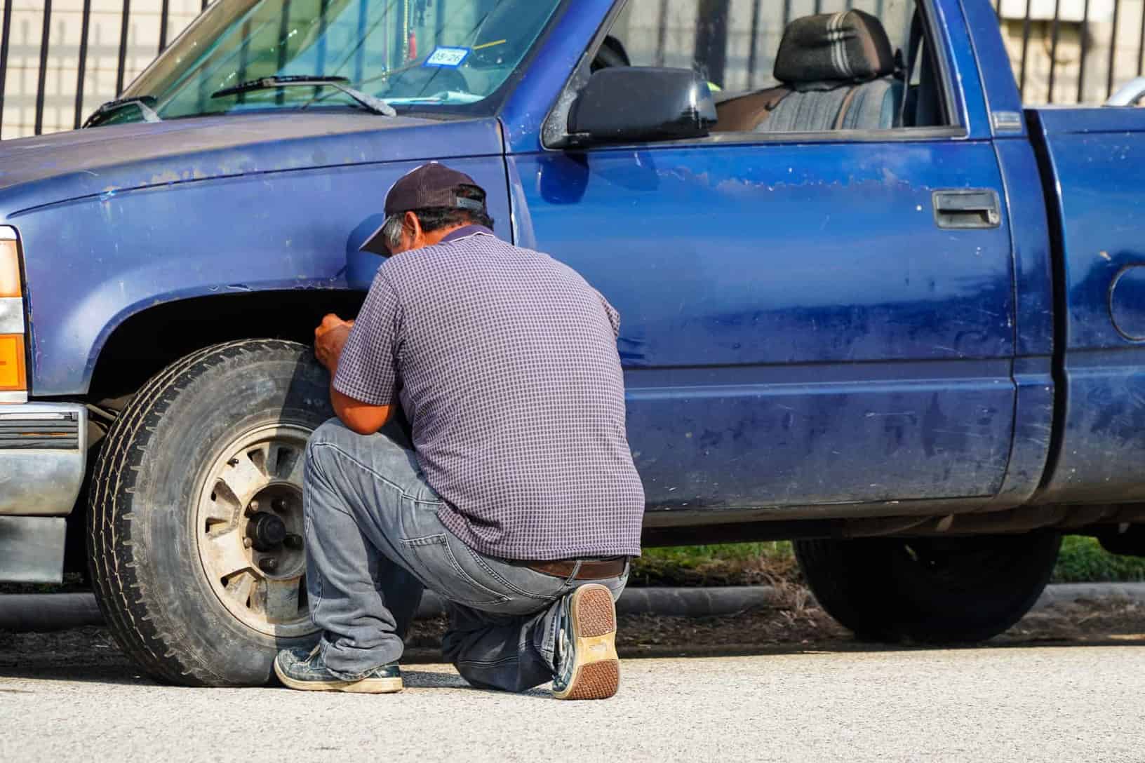 A man attentively repairing a flat tire on a blue truck in sunny Houston, Texas