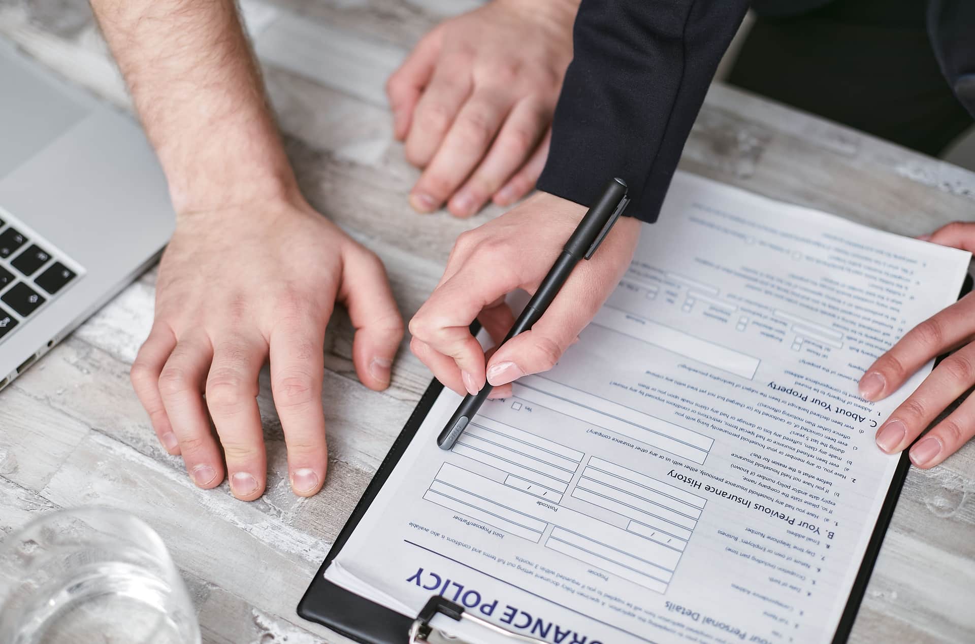 Close-up image of two people signing an insurance policy document on a wooden desk