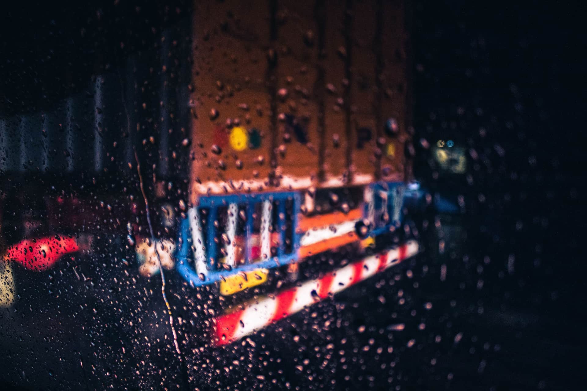 Blurred view of a truck through a rainy window at night, with water droplets on glass