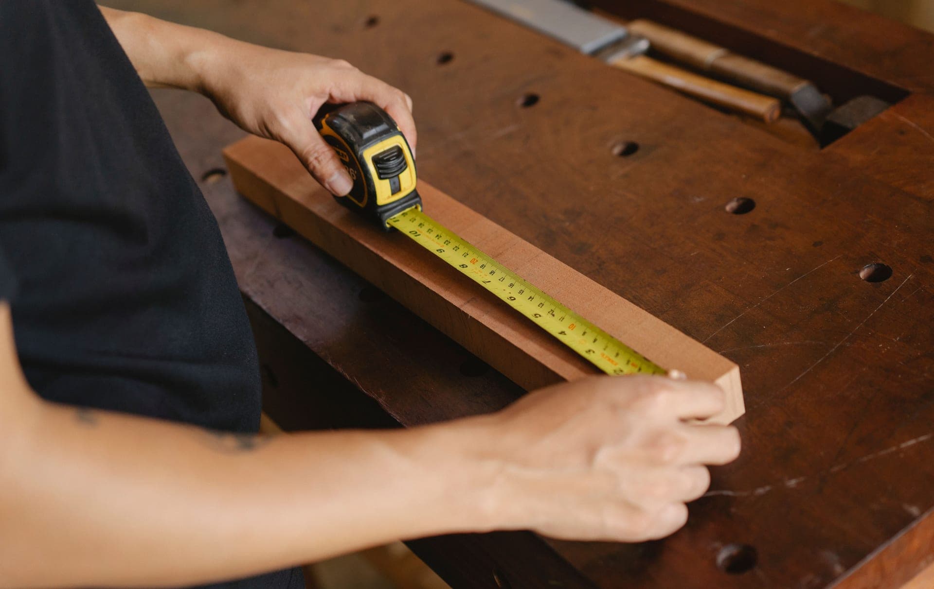 Precise unrecognizable male carpenter accurately measuring wooden detail while using ruler during work at...