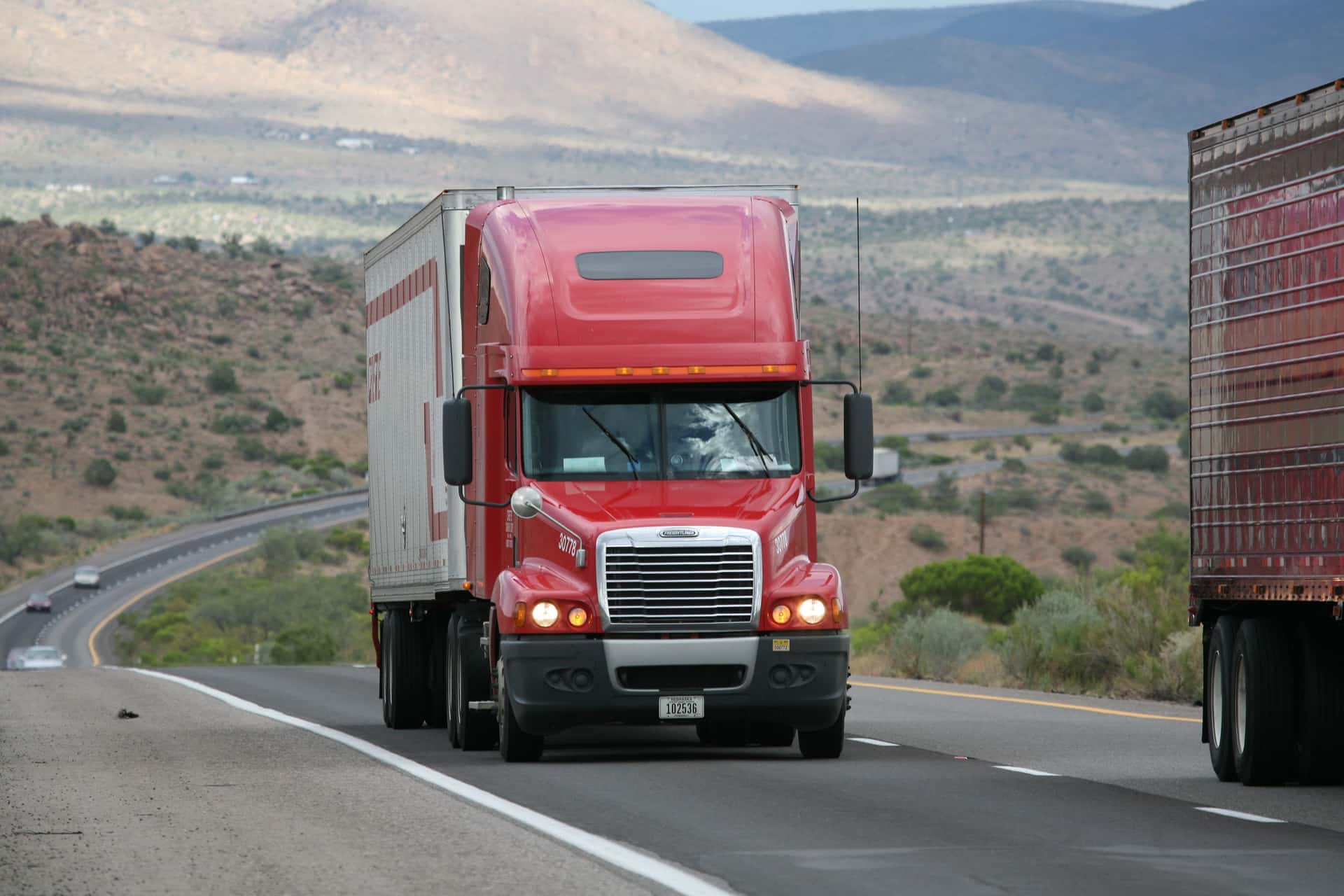 Red semi-truck driving through scenic highway in a mountainous landscape