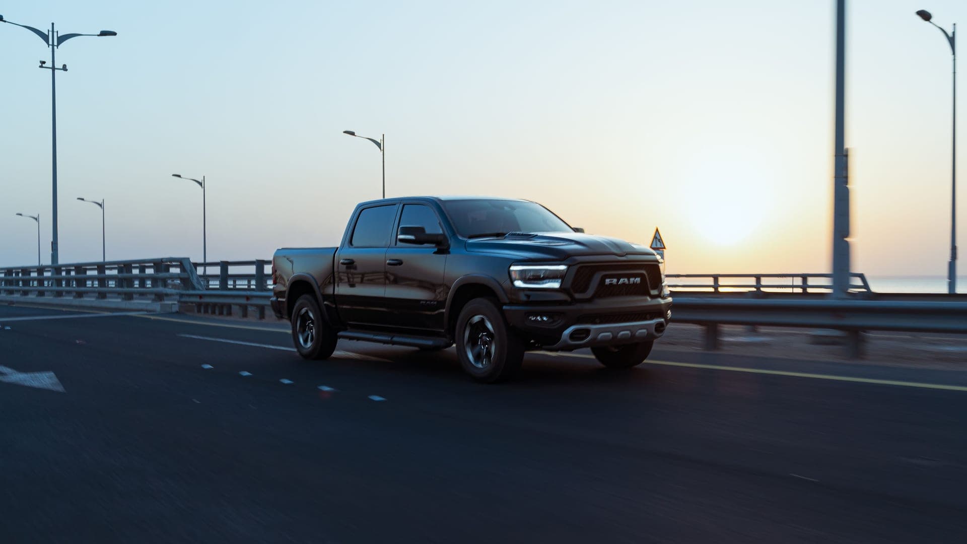 A sleek black Ram pickup truck speeds down an empty highway at sunrise