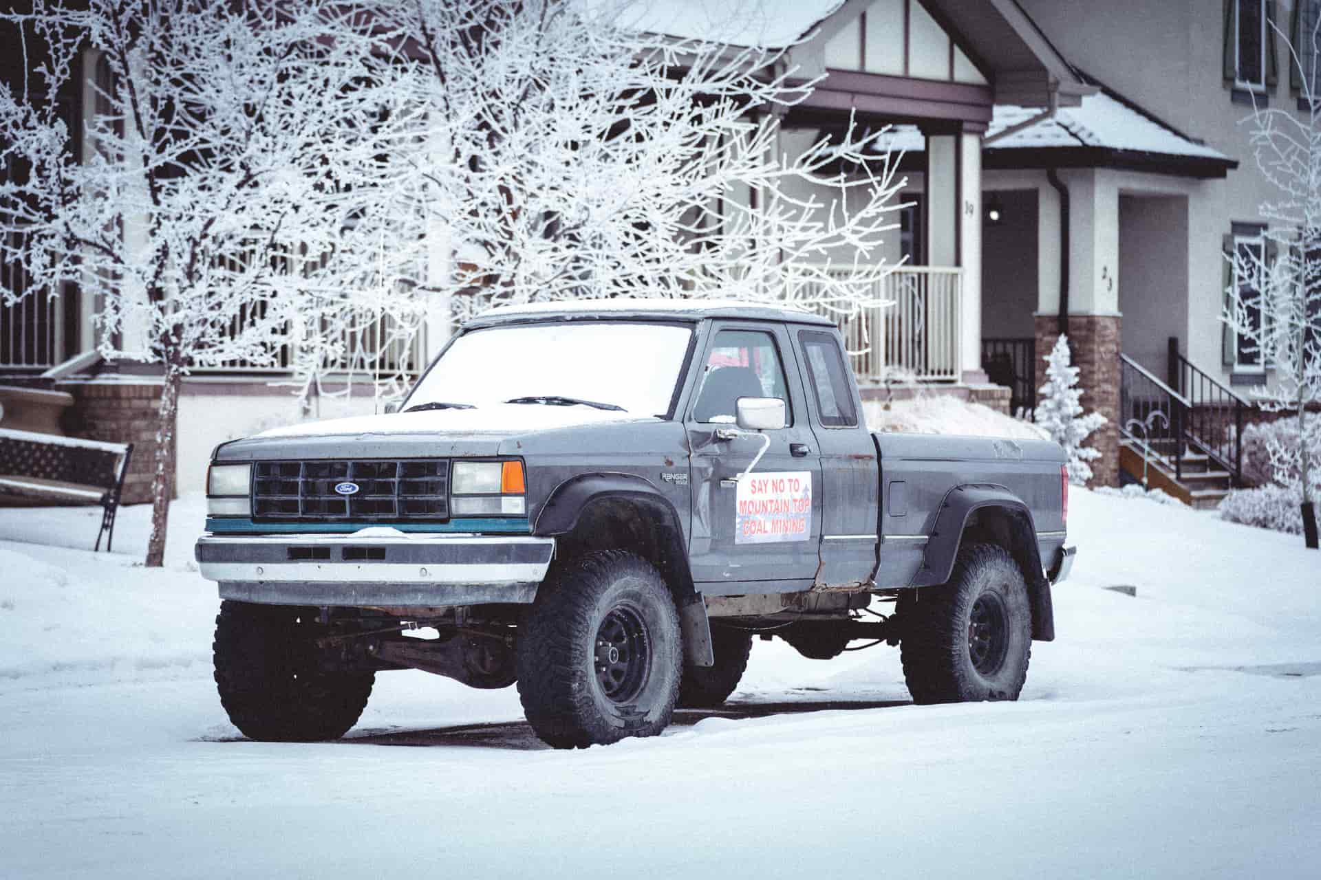 A classic Ford truck parked in a snowy, winter neighborhood