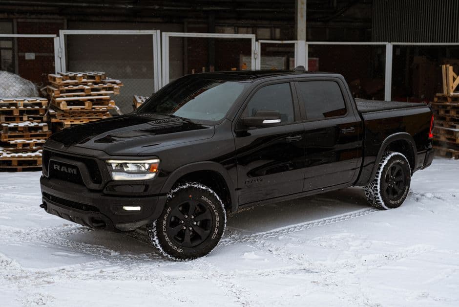 A sleek black pickup truck parked on snow in an industrial area, showcasing winter weather