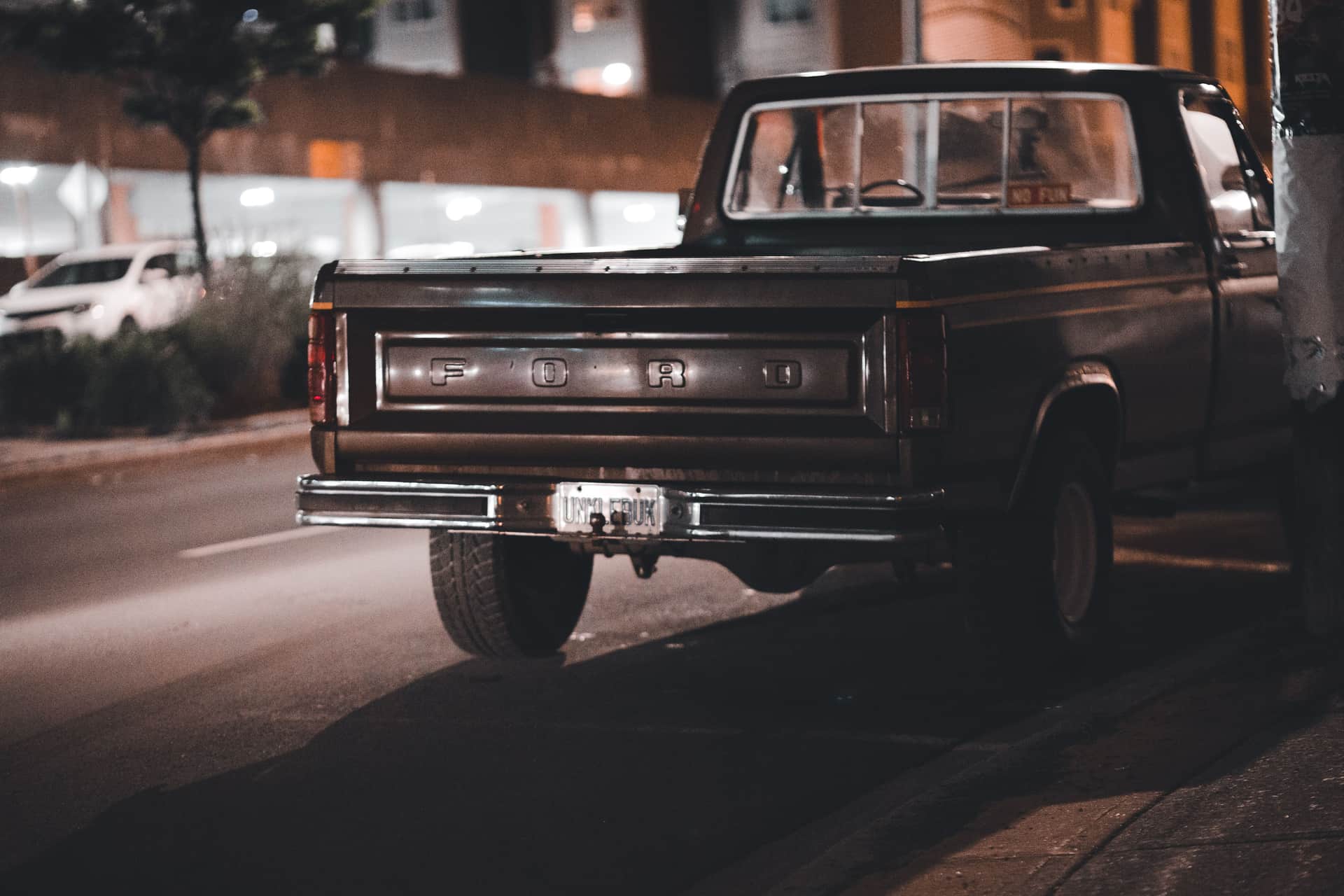 A vintage Ford pickup truck parked on a dimly-lit urban street at night