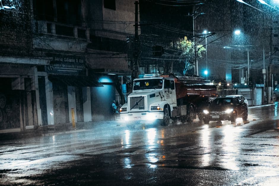 A truck and car navigate a rain-soaked city street at night, highlighting urban transportation