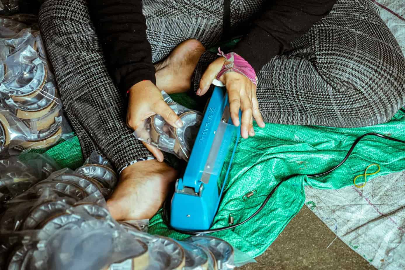 A person using a blue heat sealer to package items on a green tarp