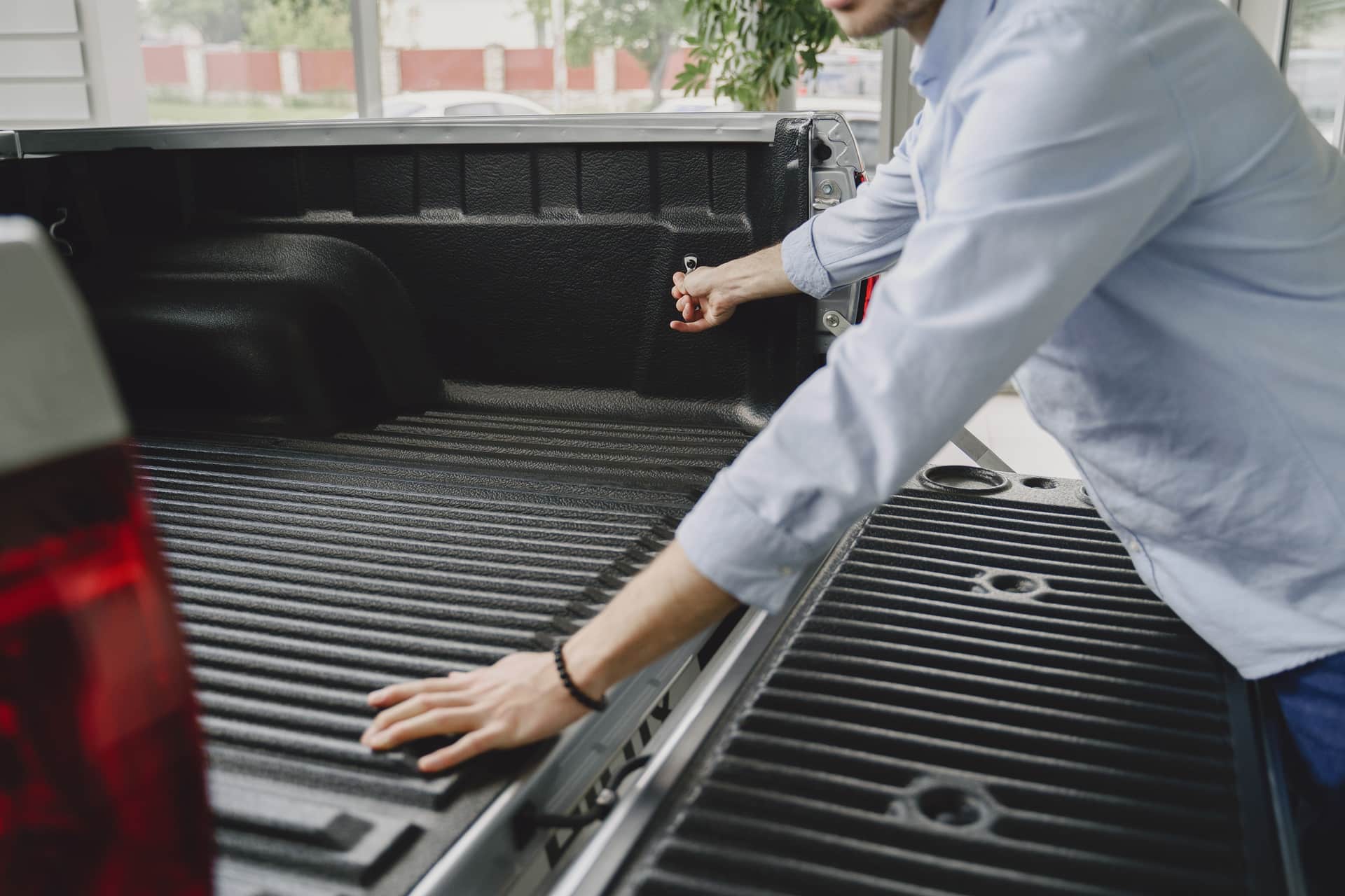 A man in a blue shirt opens the bed of a truck in a brightly lit indoor space