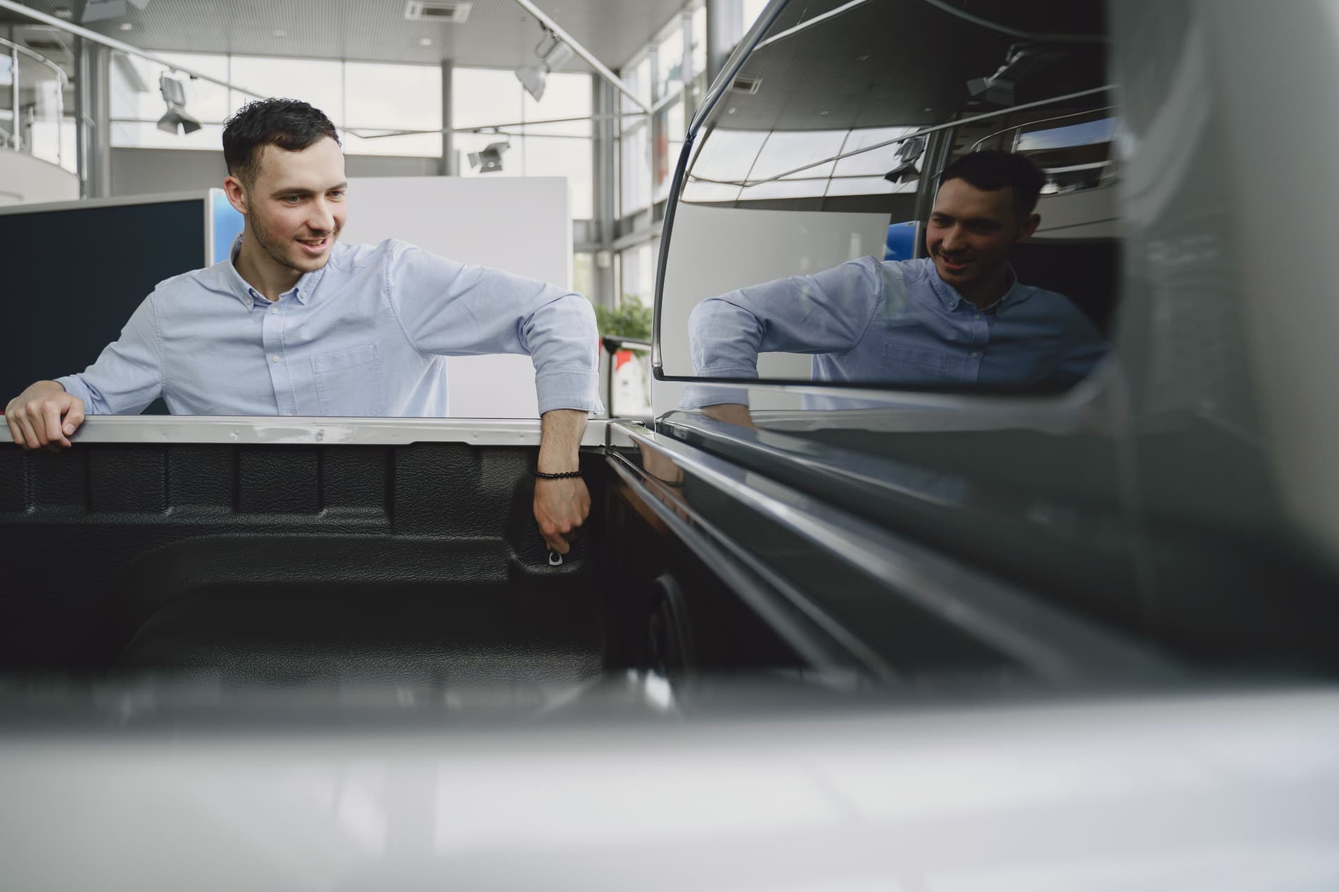 Man in a showroom examining the bed of a pickup truck, reflecting natural curiosity