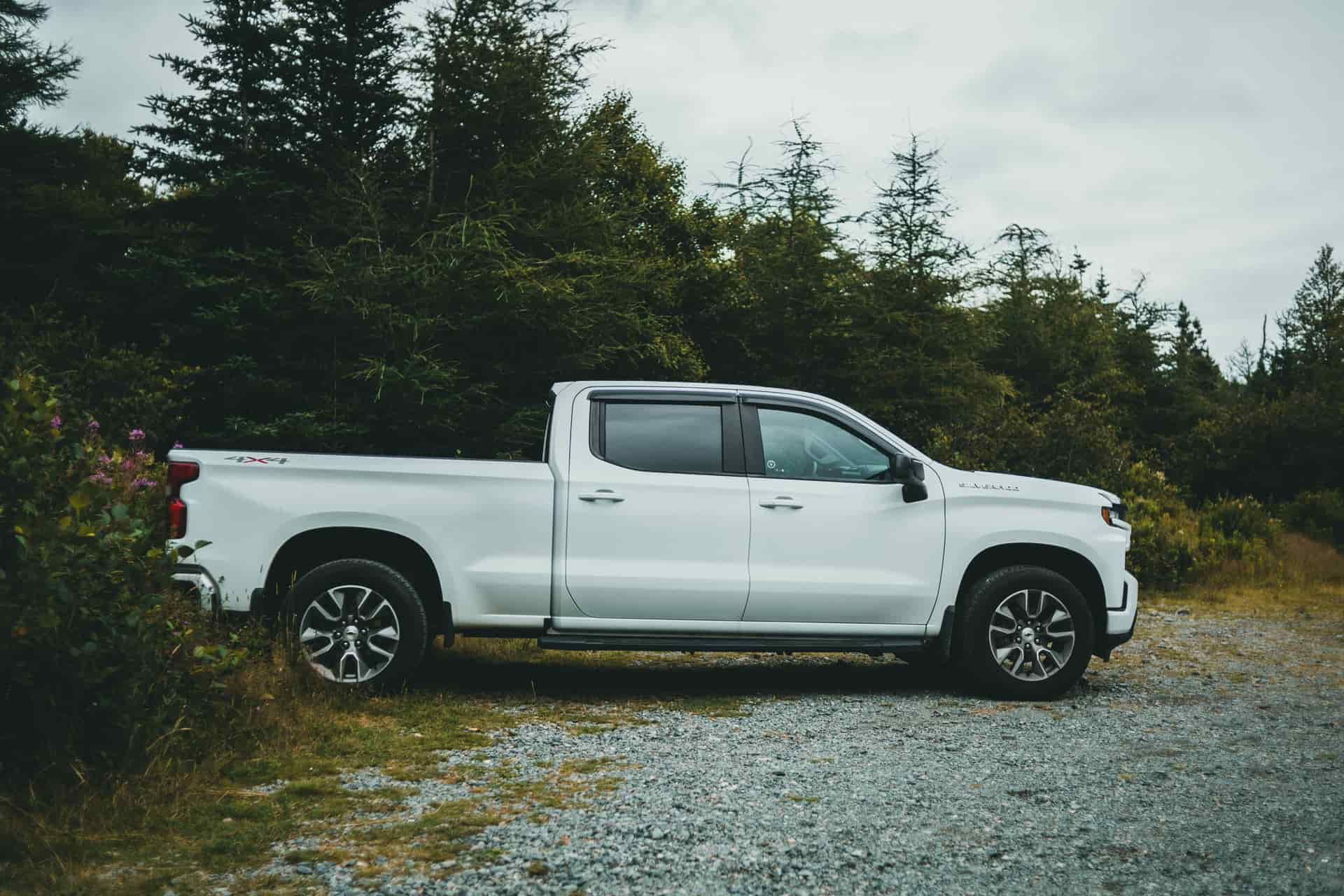A white pickup truck parked on a gravel path surrounded by green trees in a serene forest setting