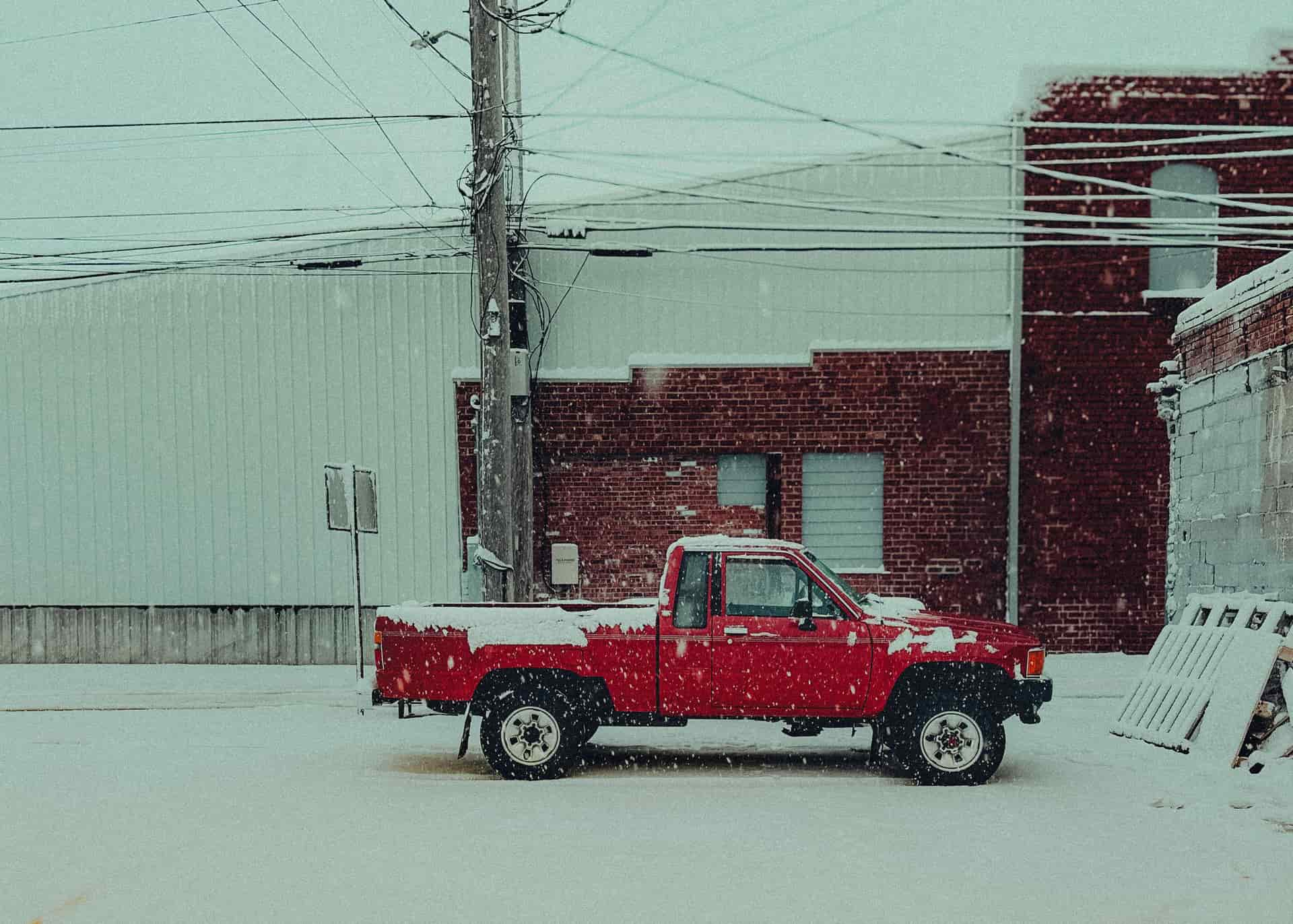 A lone red pickup truck parked in a snowy urban industrial area, capturing winter's tranquility