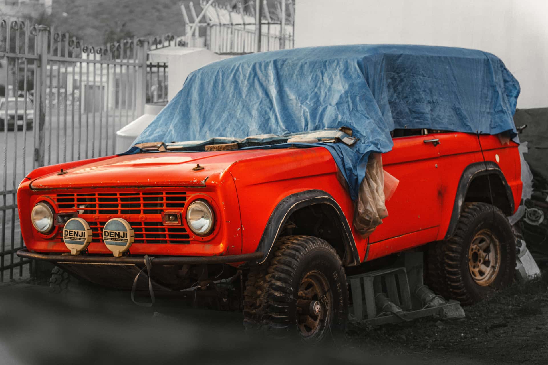 A classic red SUV covered with a blue tarp, parked outdoors