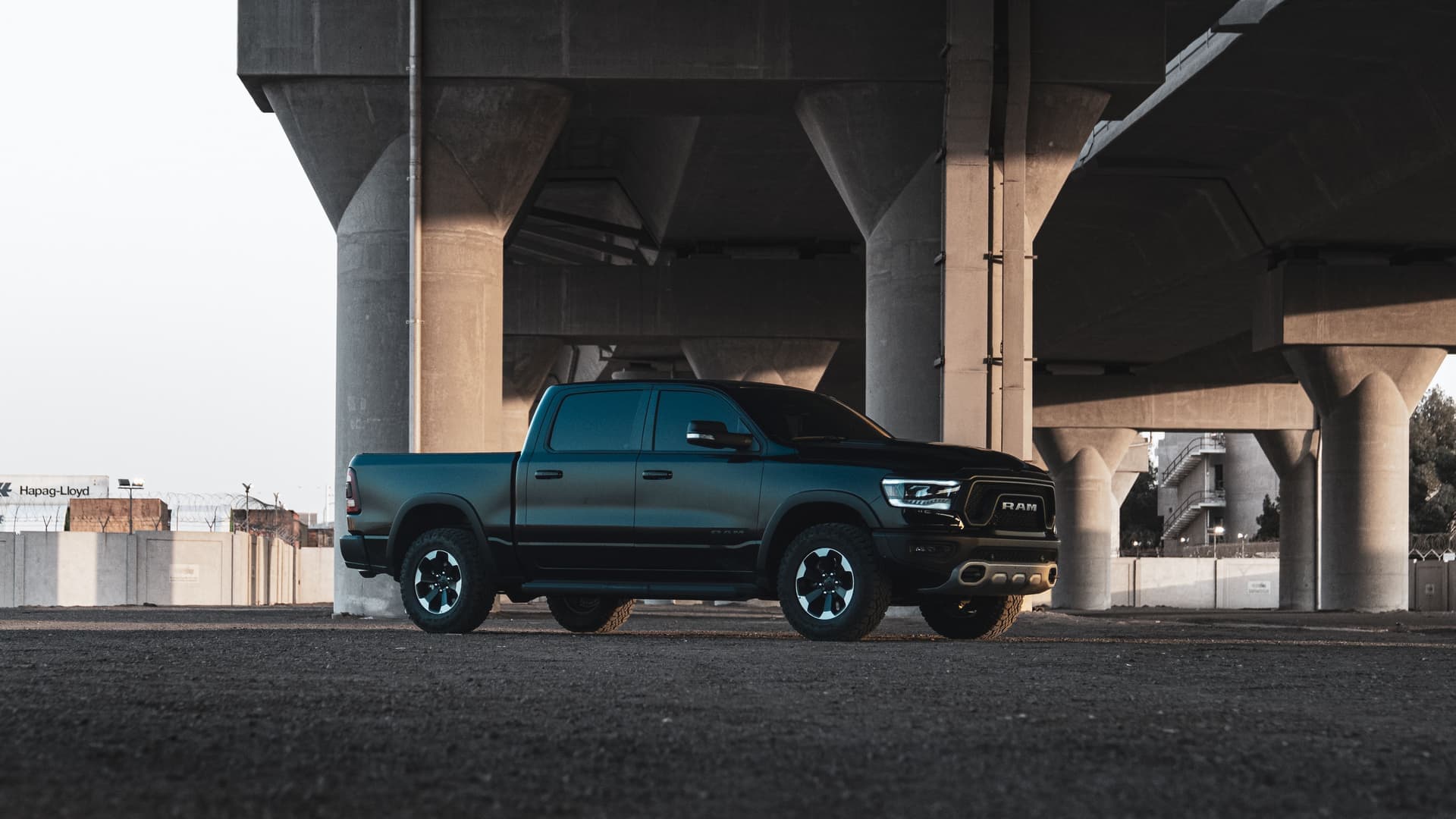 A black Ram truck parked under a concrete overpass in an urban setting