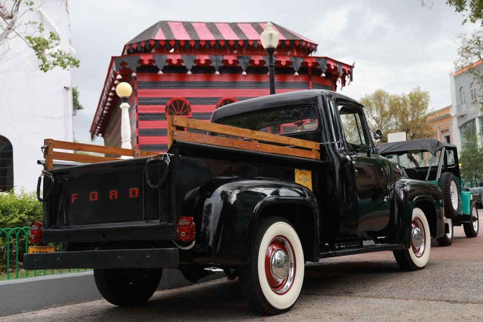 Vintage black Ford pickup truck parked outdoors with a red building backdrop