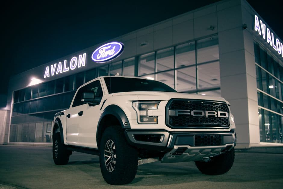 Low angle view of a modern white pickup truck with a label on the bumper, parked near a retail store