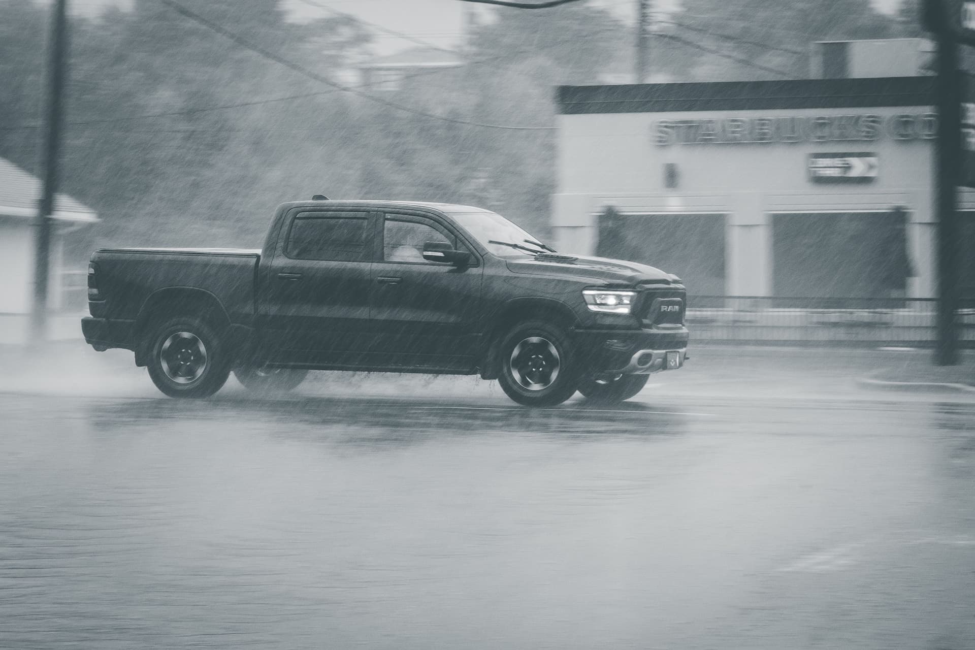 Black and white of dark pickup automobile driving on road in rainy weather on street near structure and...